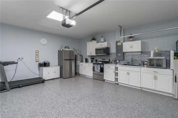 Garage with freestanding refrigerator, electric panel, electric water heater, and a garage door opener