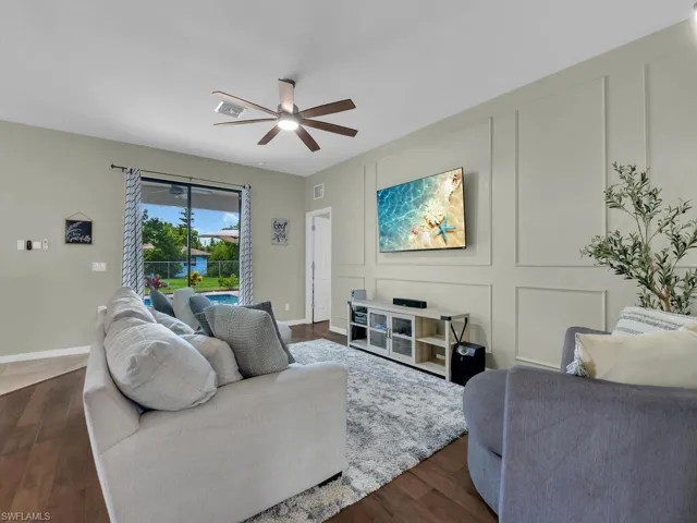 Living area with ceiling fan, dark wood-style floors, and a decorative wall