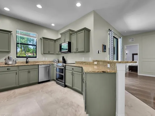 Kitchen with stainless steel appliances, green cabinets, a peninsula, light stone counters, and recessed lighting