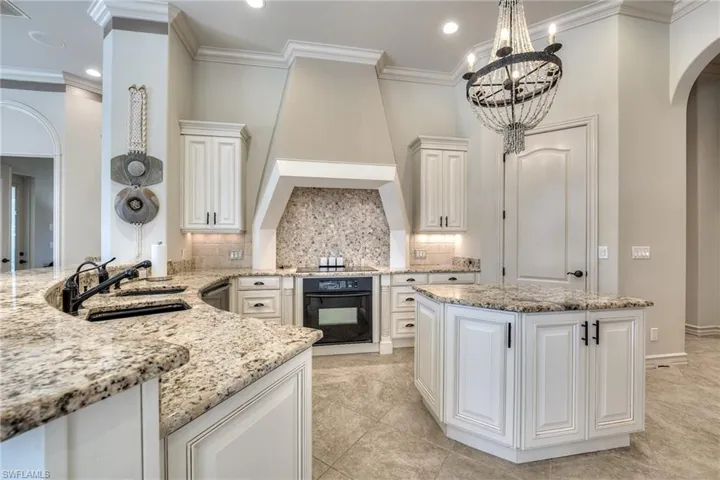 Kitchen featuring sink, light stone counters, black appliances, white cabinets, and decorative light fixtures