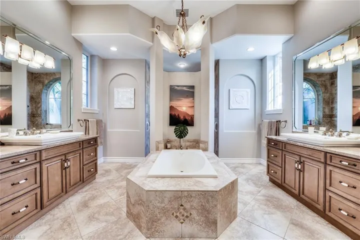 Bathroom featuring vanity, a relaxing tiled tub, and a notable chandelier