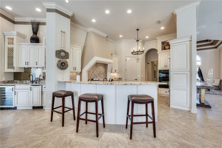 Kitchen featuring pendant lighting, wine cooler, a kitchen bar, light stone counters, and crown molding