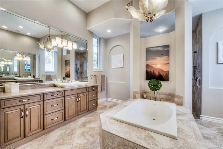 Bathroom featuring an inviting chandelier, vanity, and a relaxing tiled tub