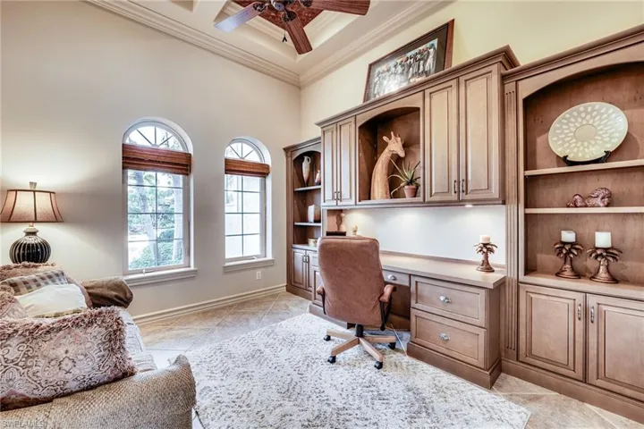 Office area featuring coffered ceiling, built in desk, ornamental molding, ceiling fan, and a high ceiling