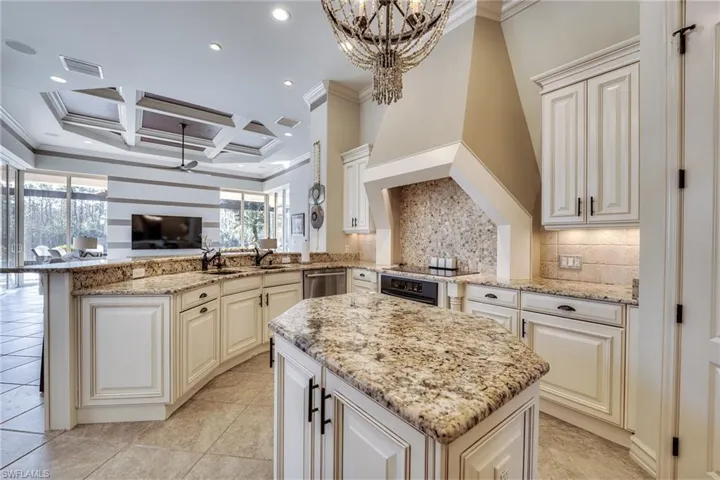 Kitchen with pendant lighting, coffered ceiling, kitchen peninsula, and light stone countertops