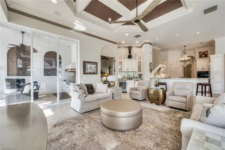 Living room featuring ornamental molding, coffered ceiling, ceiling fan with notable chandelier, and wine cooler