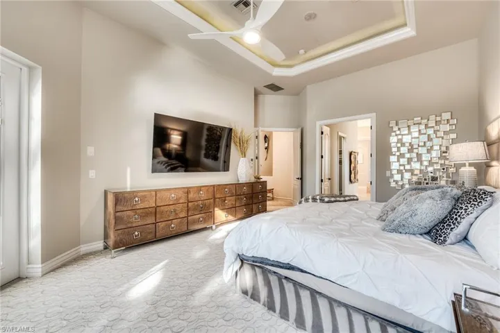 Bedroom featuring a raised ceiling, ensuite bathroom, a high ceiling, and ceiling fan