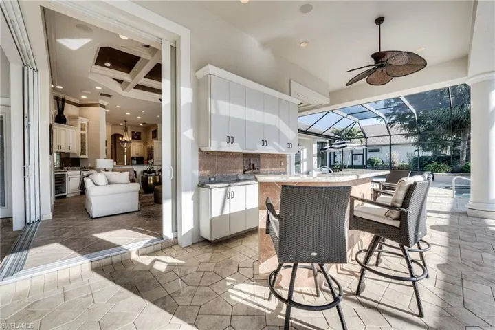 View of patio / terrace featuring a lanai, a bar, ceiling fan, beverage cooler, and exterior kitchen