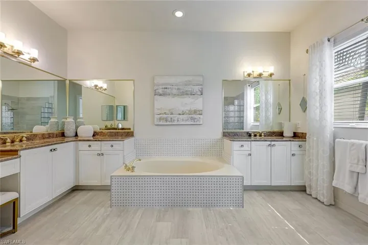 Full bath with a bath, a shower stall, two vanities, light wood-type flooring, and recessed lighting