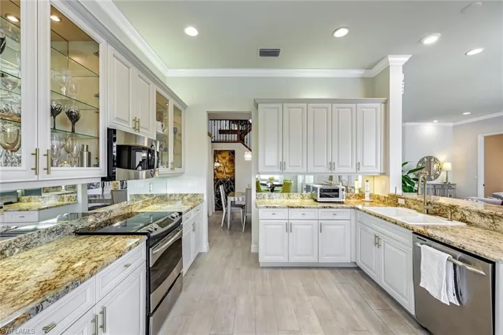 Kitchen with stainless steel appliances, crown molding, light stone counters, white cabinets, and glass insert cabinets