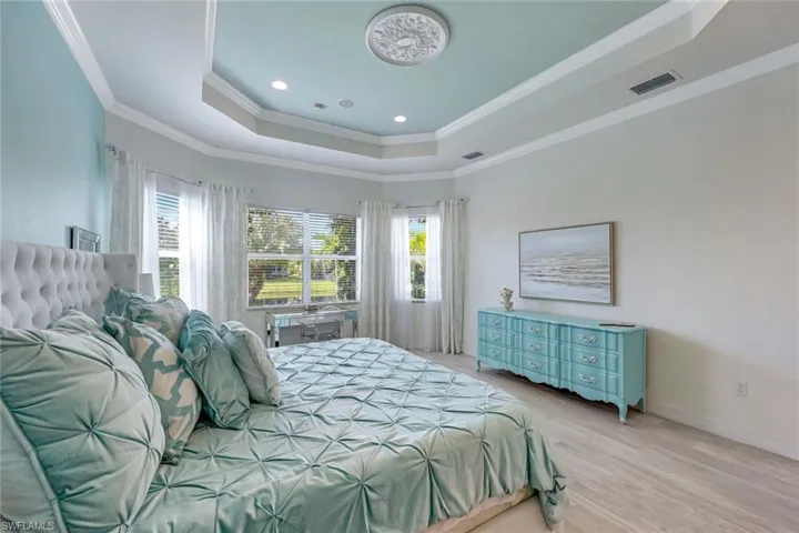 Bedroom with a tray ceiling, light wood finished floors, ornamental molding, and recessed lighting