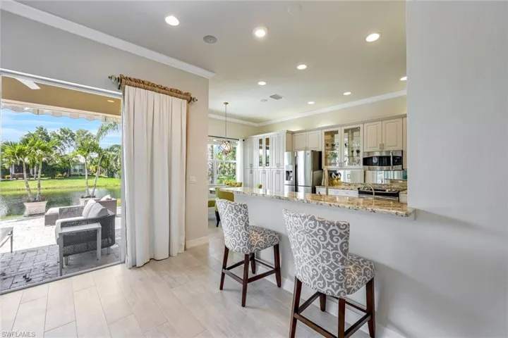 Kitchen with light stone counters, glass insert cabinets, ornamental molding, a kitchen breakfast bar, and recessed lighting