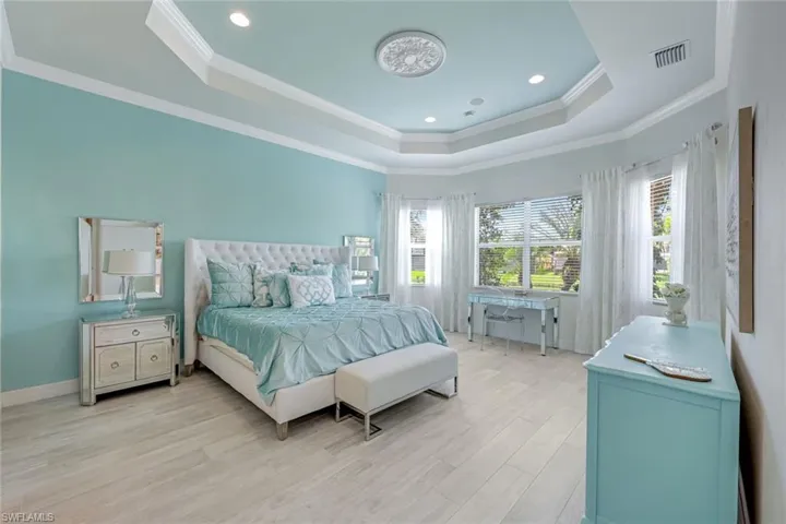 Bedroom featuring a raised ceiling, light wood finished floors, crown molding, and recessed lighting