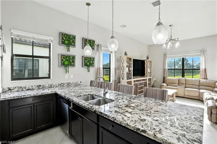 Kitchen with light stone counters, dark cabinets, a peninsula, and hanging light fixtures