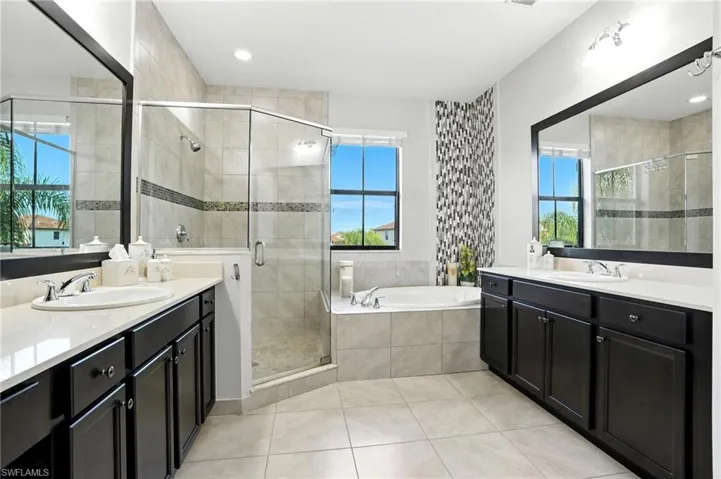 Bathroom with a stall shower, a bath, two vanities, light tile patterned floors, and recessed lighting
