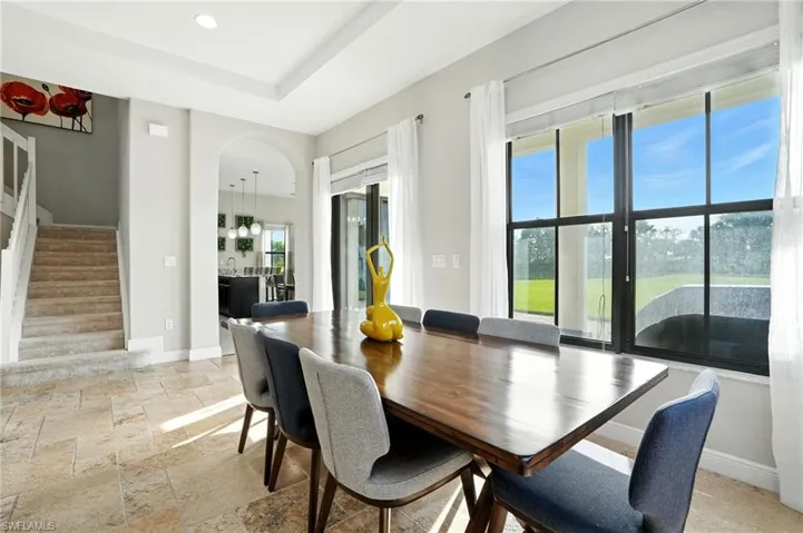Dining room with stairs, stone tile floors, arched walkways, recessed lighting, and a tray ceiling
