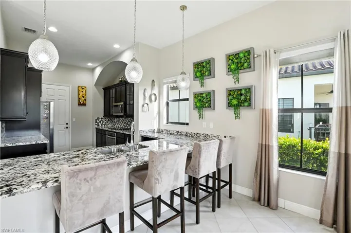 Kitchen featuring light stone countertops, dark cabinetry, a breakfast bar area, light tile patterned floors, and decorative light fixtures