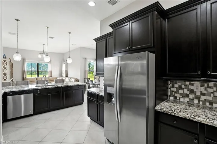 Kitchen featuring dark cabinets, stainless steel appliances, light stone counters, light tile patterned floors, and hanging light fixtures