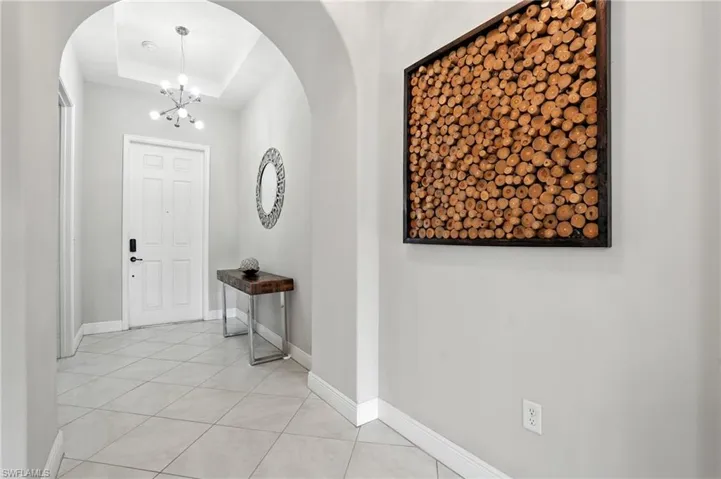 Foyer featuring arched walkways, a chandelier, light tile patterned floors, and a tray ceiling