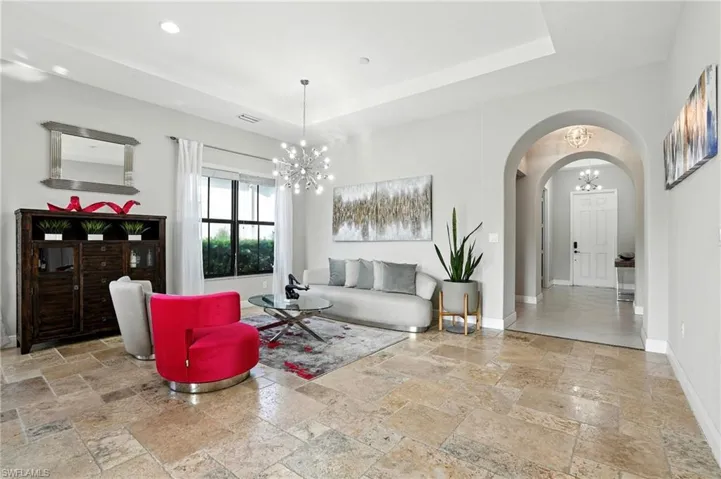 Living area featuring a chandelier, arched walkways, stone tile flooring, a raised ceiling, and recessed lighting