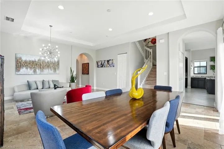 Dining area with arched walkways, a tray ceiling, stone tile floors, stairs, and a chandelier
