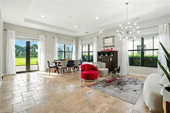 Living area featuring a tray ceiling, stone tile floors, recessed lighting, and a chandelier
