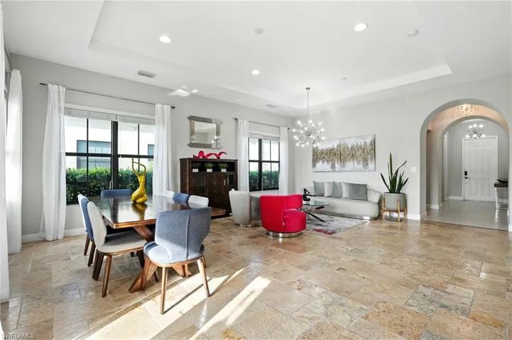 Dining area with a tray ceiling, arched walkways, a chandelier, recessed lighting, and stone tile flooring