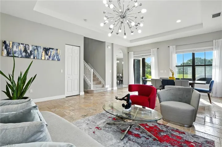 Living room with stairway, a raised ceiling, arched walkways, stone tile flooring, and recessed lighting