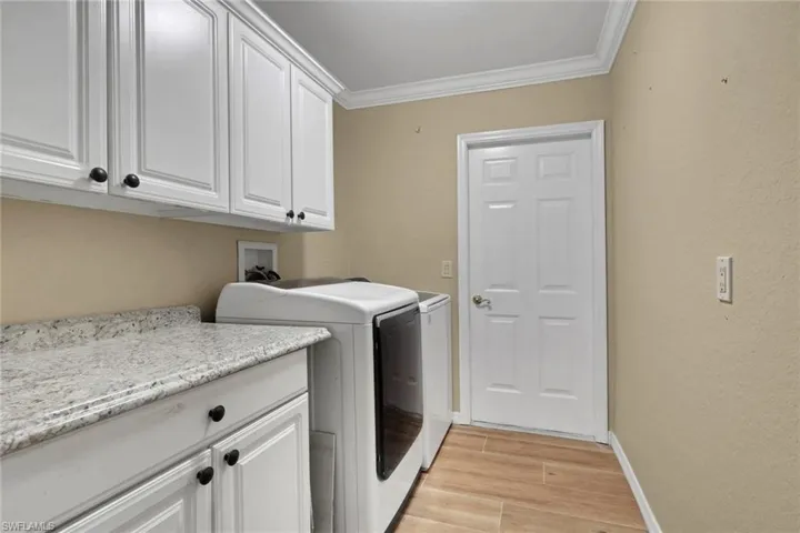 Laundry room featuring light wood-style floors, crown molding, cabinet space, and washing machine and dryer