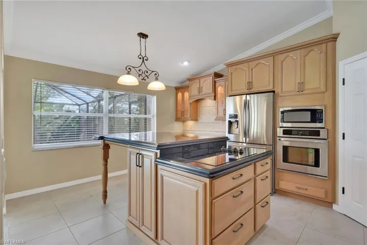 Kitchen with stainless steel appliances, dark countertops, a center island, light tile patterned flooring, and pendant lighting