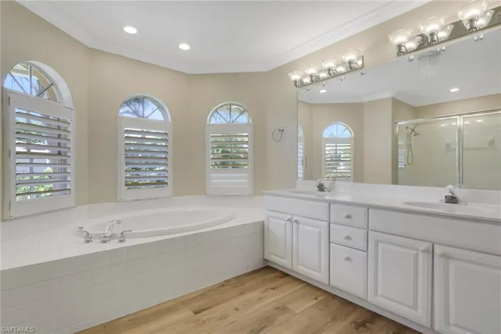 Full bathroom with double vanity, light wood-style floors, a shower stall, ornamental molding, and recessed lighting