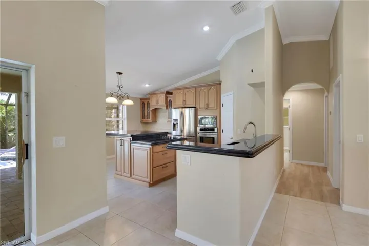 Kitchen with a peninsula, lofted ceiling, light tile patterned floors, a kitchen island, and arched walkways
