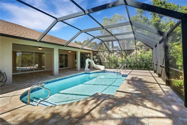 Swimming pool featuring a patio area, a sunroom, glass enclosure, and a water slide
