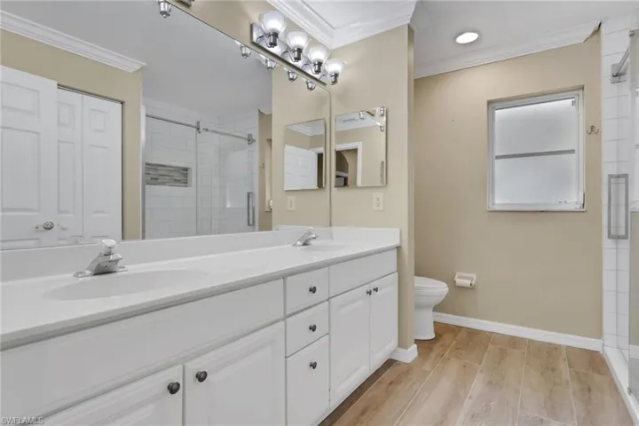 Bathroom with double vanity, crown molding, light wood-style floors, a stall shower, and a closet