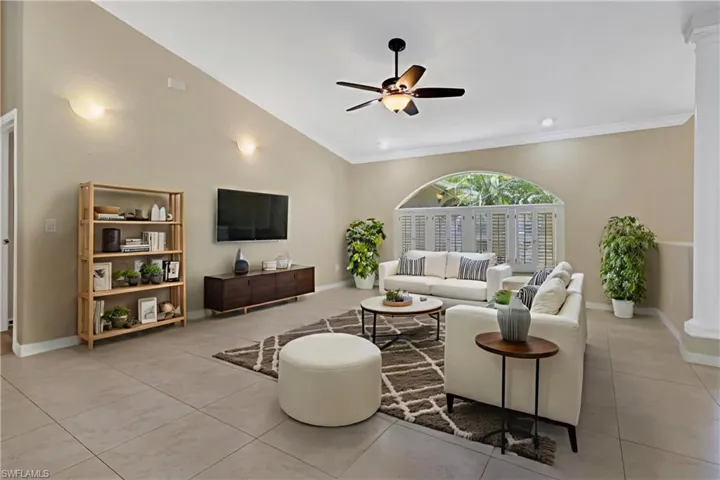 Living room featuring ceiling fan, light tile patterned floors, crown molding, and ornate columns