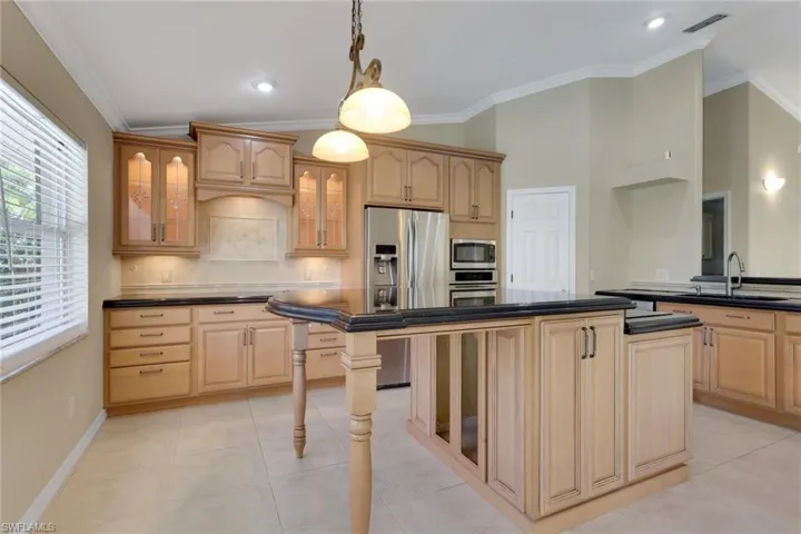 Kitchen with glass fronted cabinets, a center island, vaulted ceiling, ornamental molding, and decorative light fixtures