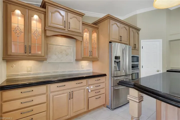 Kitchen featuring glass fronted cabinets, light wood finish cabinets, stainless steel appliances, backsplash, and dark stone counters