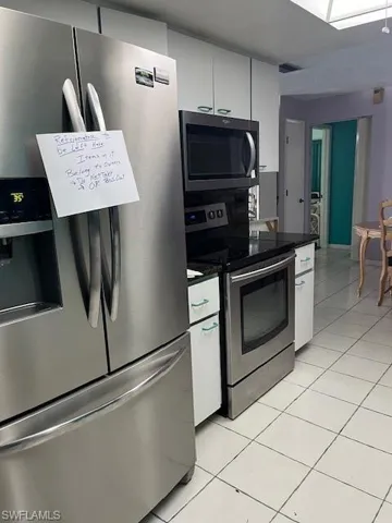 Kitchen featuring light tile floors, white cabinetry, stainless steel fridge with ice dispenser, and range
