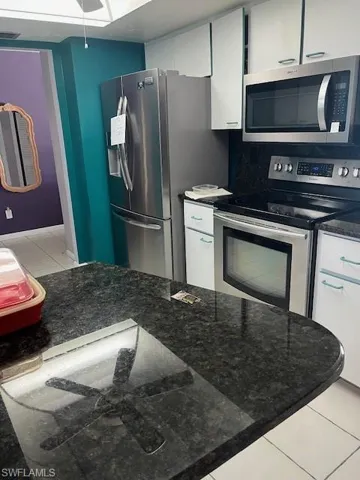 Kitchen with dark stone counters, fridge, range, white cabinets, and light tile floors