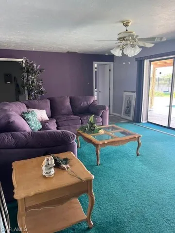 Living room with carpet flooring, ceiling fan, and a textured ceiling