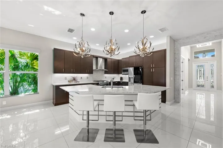 Kitchen with visible vents, appliances with stainless steel finishes, a sink, wall chimney range hood, and an inviting chandelier