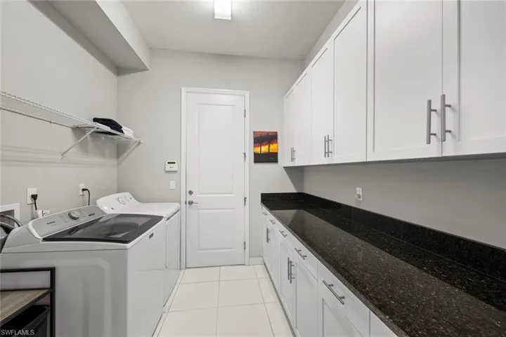 Laundry area with light tile patterned flooring, washing machine and dryer, and cabinet space