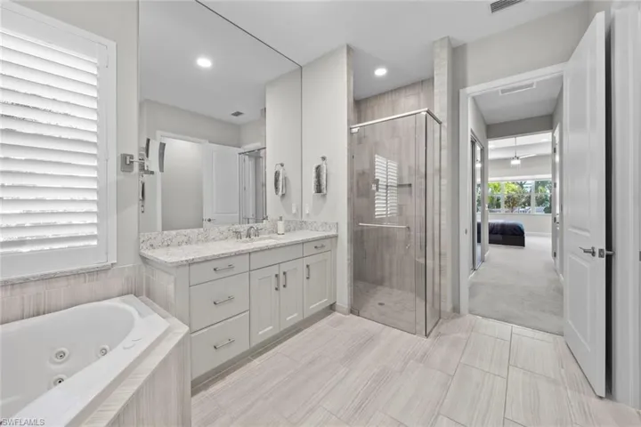 Full bath featuring visible vents, a tub with jets, recessed lighting, vanity, and a stall shower