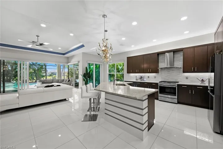 Kitchen with open floor plan, stainless steel gas range oven, freestanding refrigerator, a sink, and wall chimney range hood