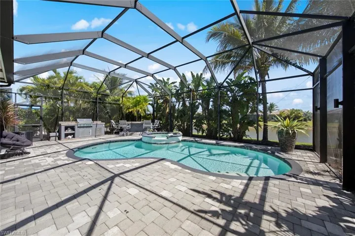 View of swimming pool with a patio, a pool with connected hot tub, an outdoor kitchen, and glass enclosure