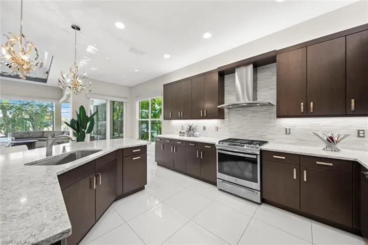 Kitchen with decorative backsplash, stainless steel range with gas stovetop, wall chimney exhaust hood, a sink, and a notable chandelier