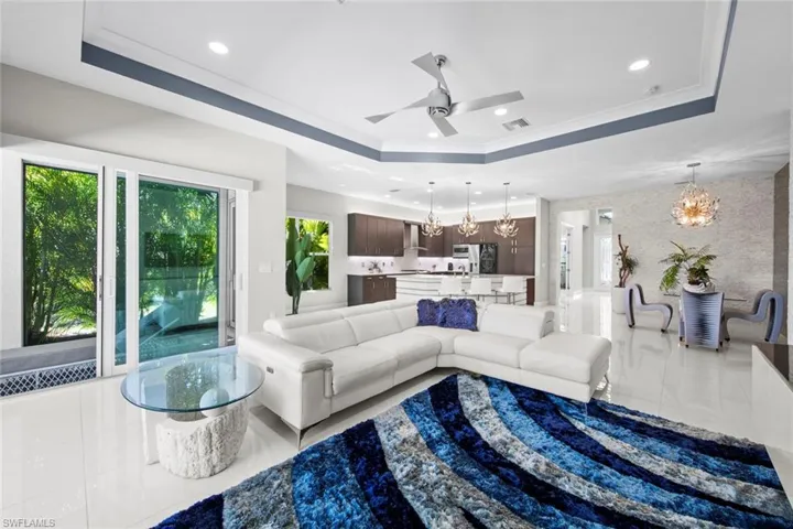 Living area with recessed lighting, ceiling fan with notable chandelier, and a raised ceiling