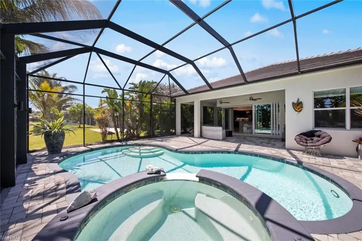 View of swimming pool featuring glass enclosure, a pool with connected hot tub, and a patio area