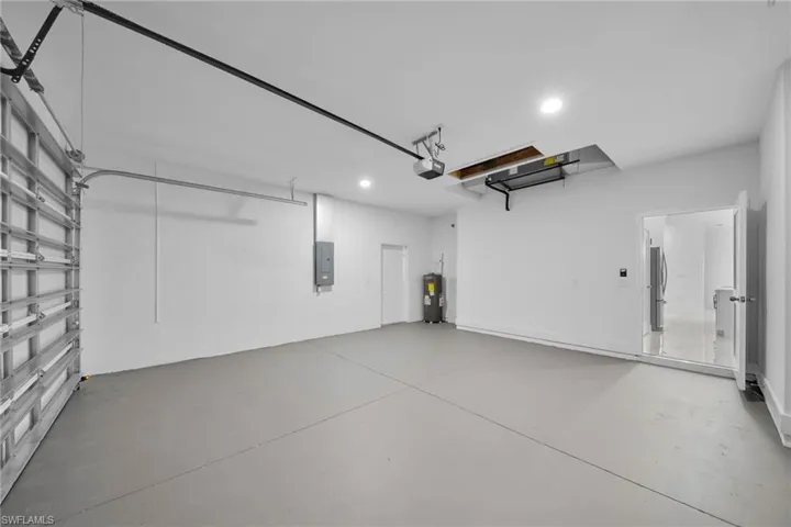 Garage with electric water heater, stainless steel refrigerator, a garage door opener, and electric panel