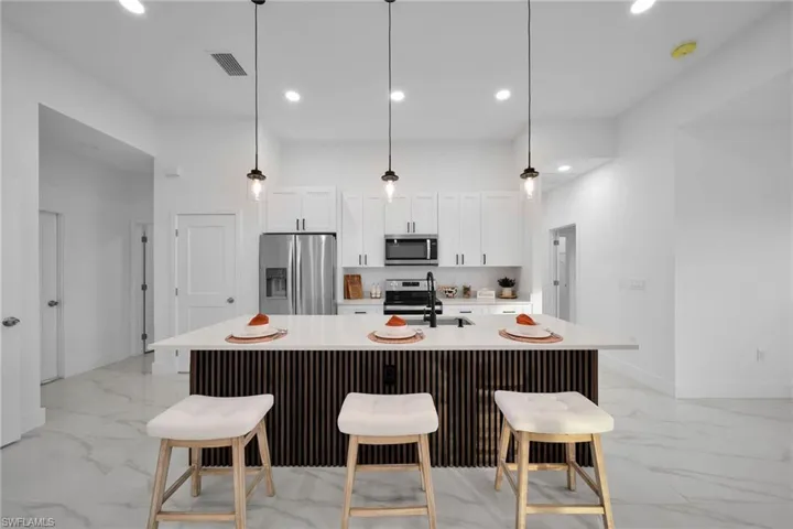 Virtually Staging Kitchen featuring white cabinetry, pendant lighting, appliances with stainless steel finishes, and an island with sink